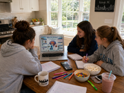 Three people sitting around a table with a laptop, snacks, and stationery in a kitchen.