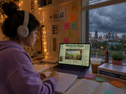 Person studying with a laptop and headphones, cityscape visible through window