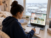 Person sitting at a desk with a laptop and notebook, looking out a window with a snowy view.